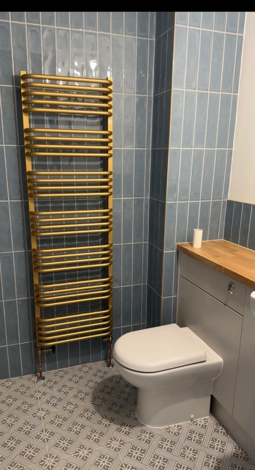 Blue tiled bathroom with brass towel rail and patterned floor