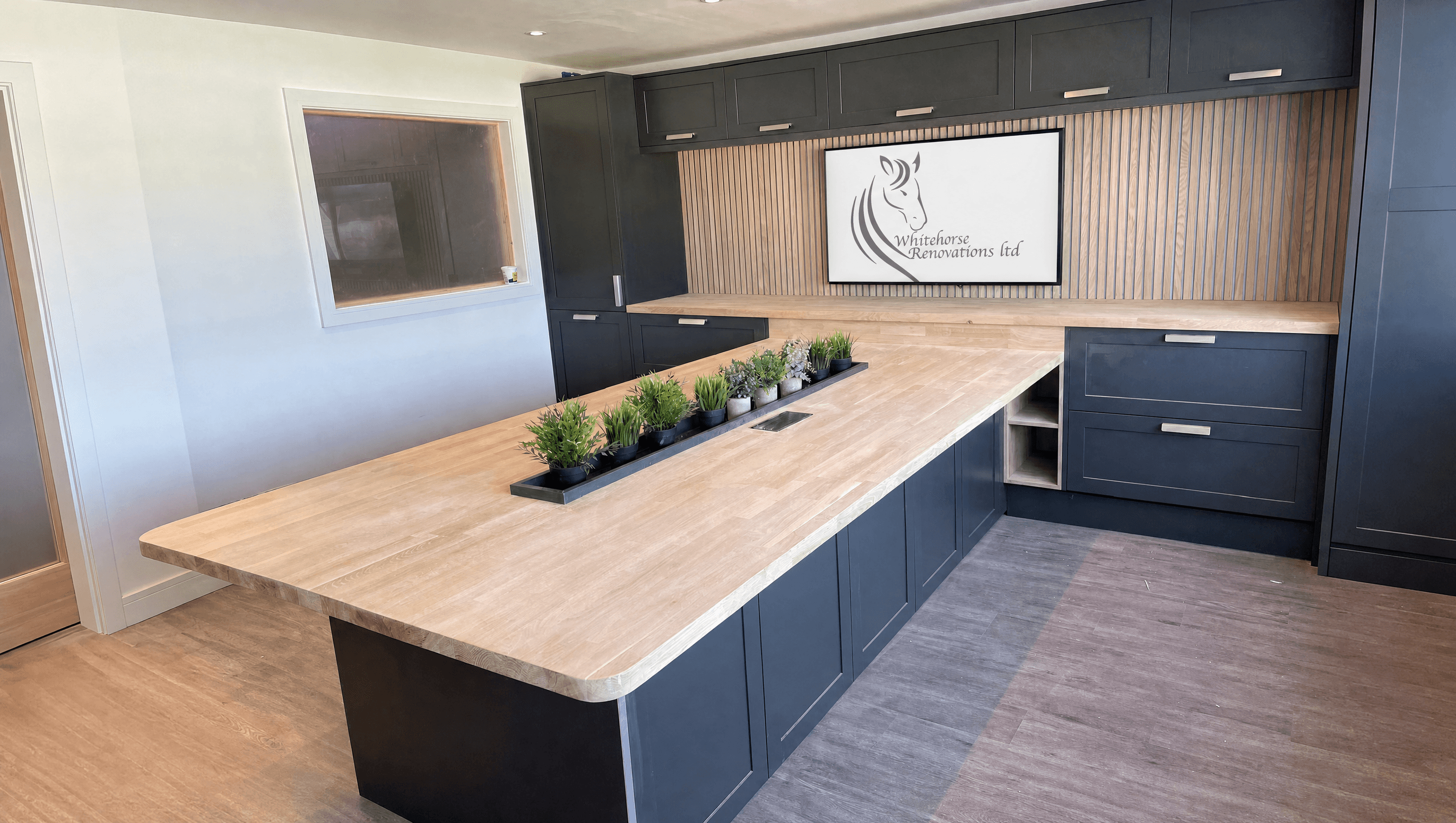 Navy kitchen island with oak worktop and wall-mounted screen