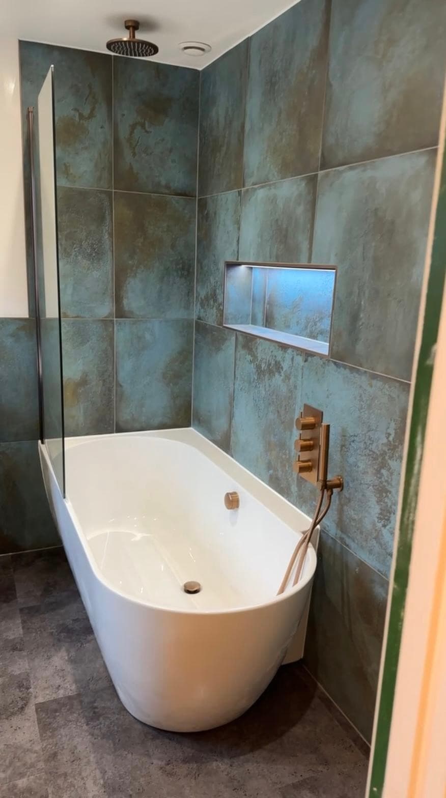 Freestanding bath with brass fittings against oxidised teal tile